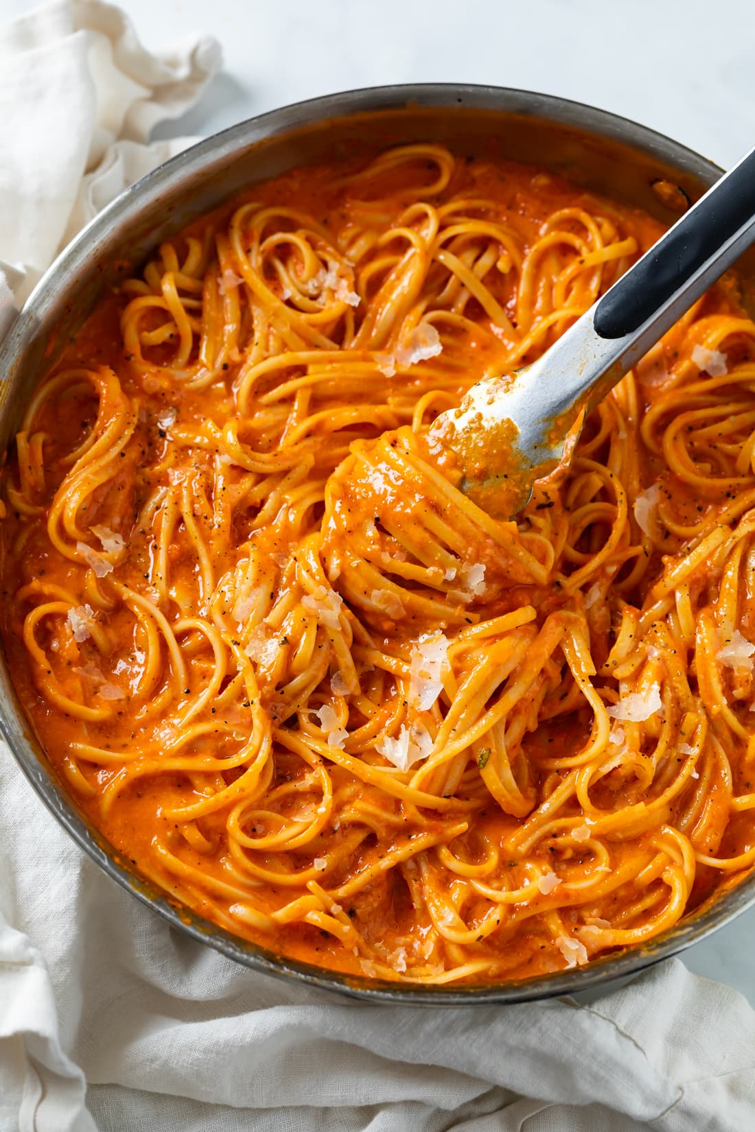 Roasted Red Pepper Pasta in a skillet with kitchen tongs scooping it up.