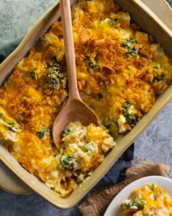 A casserole dish filled with chicken broccoli rice casserole with a wooden spoon in it.