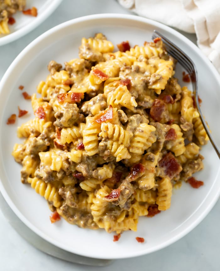 A white plate topped with cheeseburger pasta with ground beef and bacon in a creamy cheese sauce.