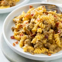 A white plate with Cheeseburger Pasta in a creamy cheese sauce with seasoned beef and bacon.