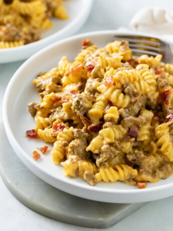 A white plate with Cheeseburger Pasta in a creamy cheese sauce with seasoned beef and bacon.