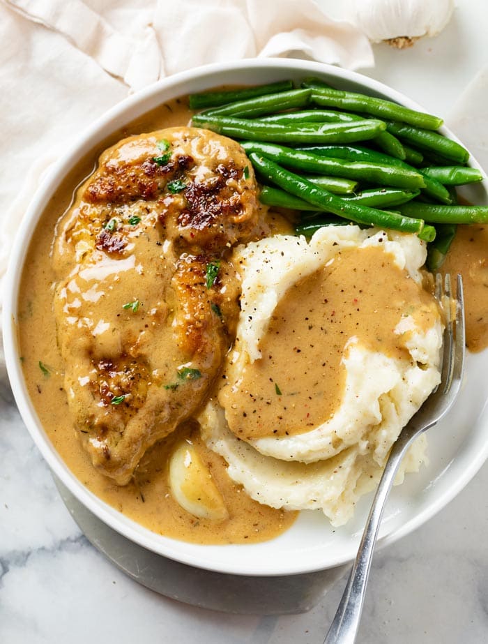 A white plate with Creamy Garlic Chicken, Mashed Potatoes, Green Beans, and Gravy.