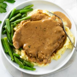 Pork Chops and Gravy on top of a pile of mashed potatoes with green beans on the side.