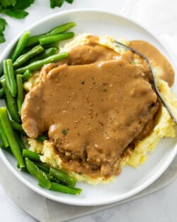 Pork Chops and Gravy on top of a pile of mashed potatoes with green beans on the side.