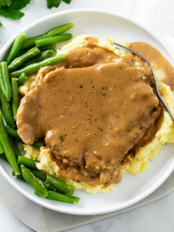 Pork Chops and Gravy on top of a pile of mashed potatoes with green beans on the side.