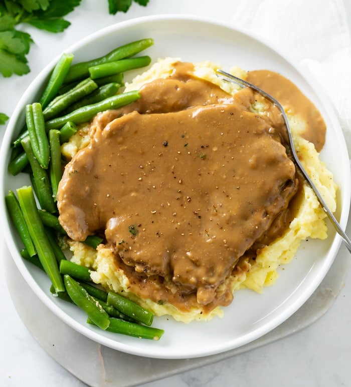 Pork Chops and Gravy on top of a pile of mashed potatoes with green beans on the side.