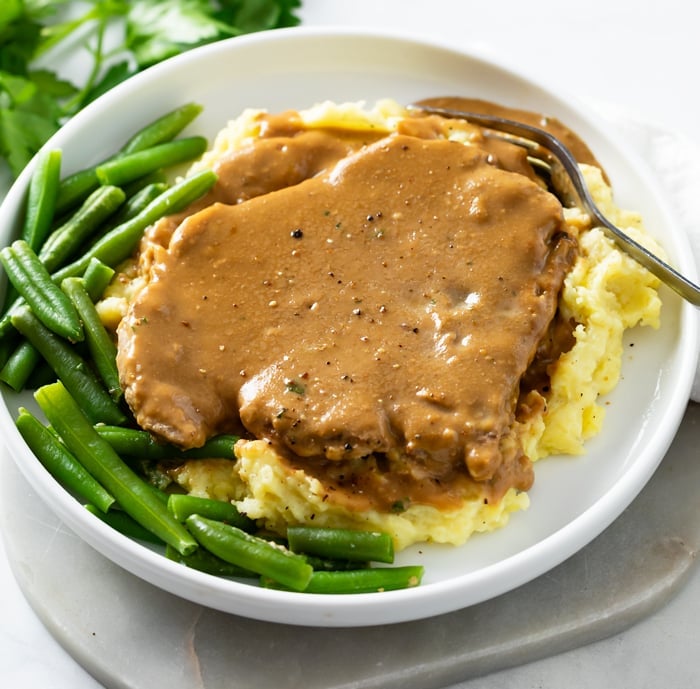 Crock Pot Pork Chops smothered in gravy on top of mashed potatoes with green beans on the side.