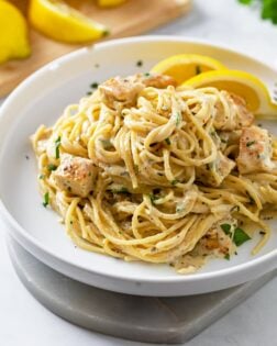 A white plate of creamy lemon chicken pasta with lemon slices and fresh parsley.