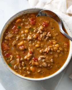 A bowl of Lentil Sausage Soup with a spoon on the side.