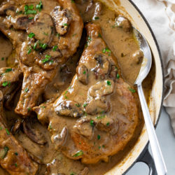 A skillet with Mushroom Pork Chops with a gravy sauce and fresh parsley.