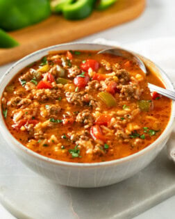 A bowl of Stuffed Pepper Soup with a spoon in it and bell peppers in the background.