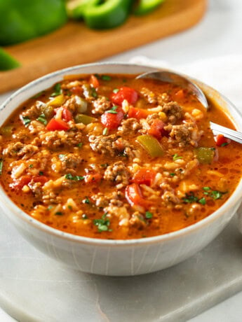 A bowl of Stuffed Pepper Soup with a spoon in it and bell peppers in the background.