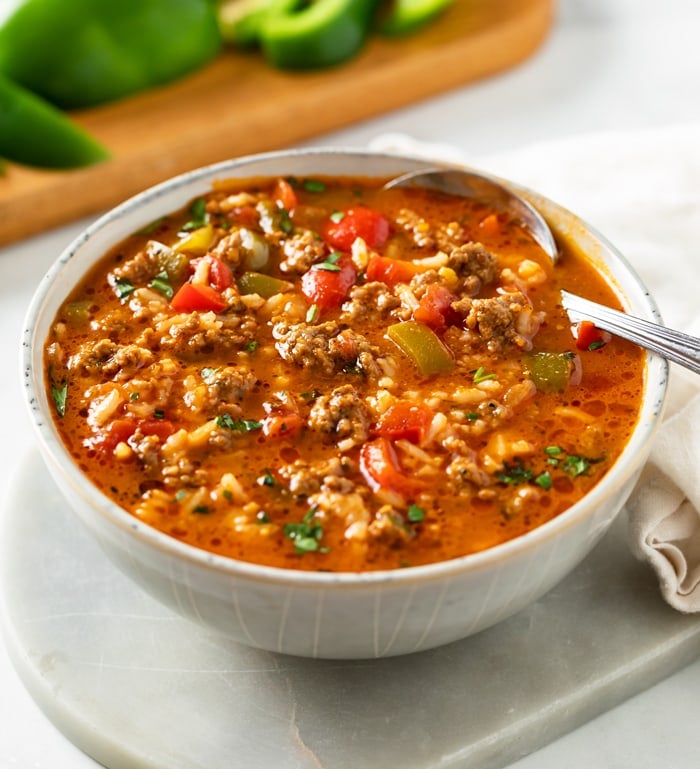 A bowl of Stuffed Pepper Soup with a spoon in it and bell peppers in the background.