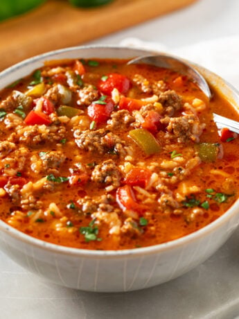 A white bowl filled with Stuffed Pepper Soup with a spoon on the side.