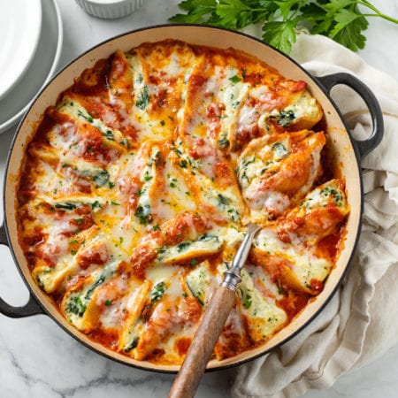 A pot filled with cheesy stuffed shells with fresh parsley on the side.