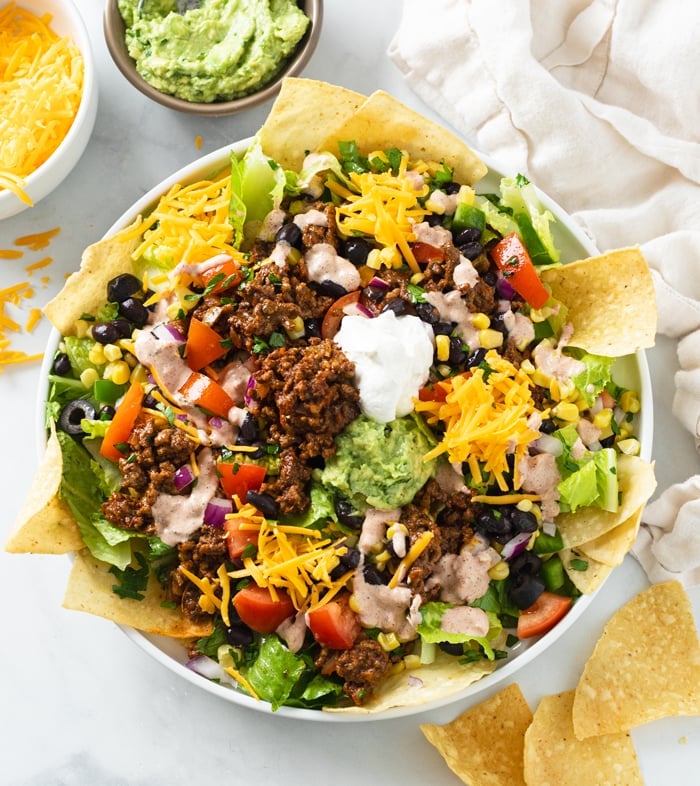 A white plate filled with Taco Salad with seasoned ground beef, cheese, tortilla chips, and more.