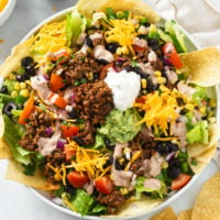 A Taco Salad on a white plate with seasoned ground beef, dressing, sour cream, and vegetables.