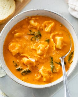 A white bowl with creamy Tomato Tortellini Soup in it with spinach.