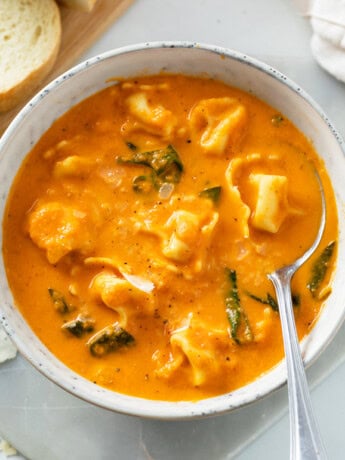 A white bowl with creamy Tomato Tortellini Soup in it with spinach.