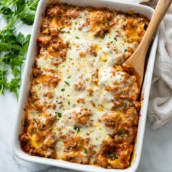 Baked Ravioli in a white baking dish with a wooden spoon on the side.