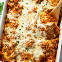 Baked Ravioli in a casserole dish with a wooden spoon and parsley.