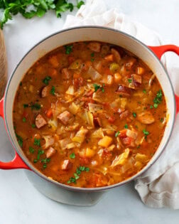 A red Dutch oven filled with Cabbage Soup with vegetables and Kielbasa.