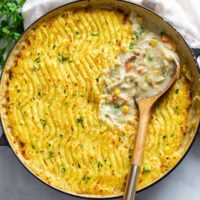 A skillet filled with Chicken Shepherd's Pie with a wooden spoon scooping up the filling.