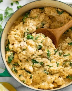 A dutch oven with Creamy Chicken and Rice with Spinach and a wooden spoon scooping it up.