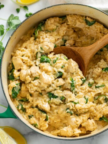 A dutch oven with Creamy Chicken and Rice with Spinach and a wooden spoon scooping it up.