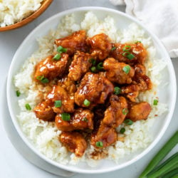 Firecracker Chicken on a bed of white rice with green onions on top.