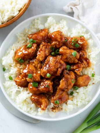 Firecracker Chicken on a bed of white rice with green onions on top.