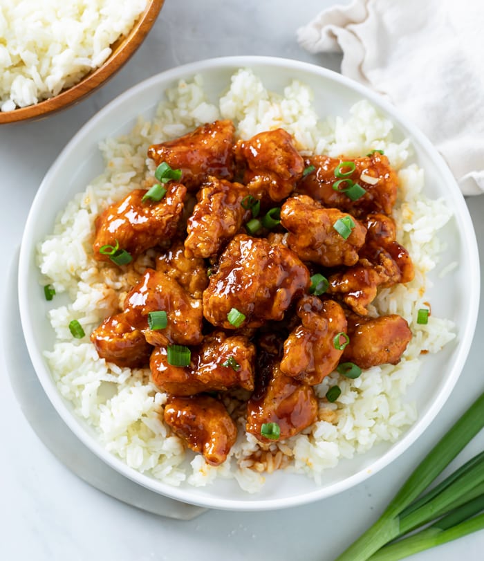 Firecracker Chicken on a bed of white rice with green onions on top.
