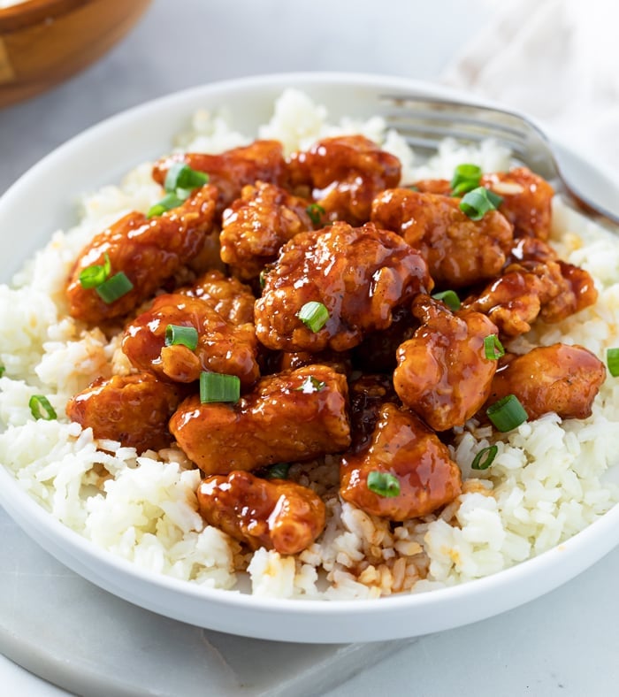 A white plate of Firecracker Chicken with green onions on top.
