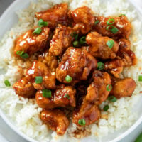 A bed of rice topped with Firecracker Chicken with sliced green onions on top.