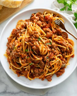 Spaghetti topped with Meat Sauce on a white plate with a fork and parsley on top.