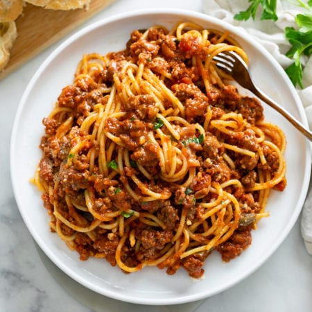Spaghetti topped with Meat Sauce on a white plate with a fork and parsley on top.