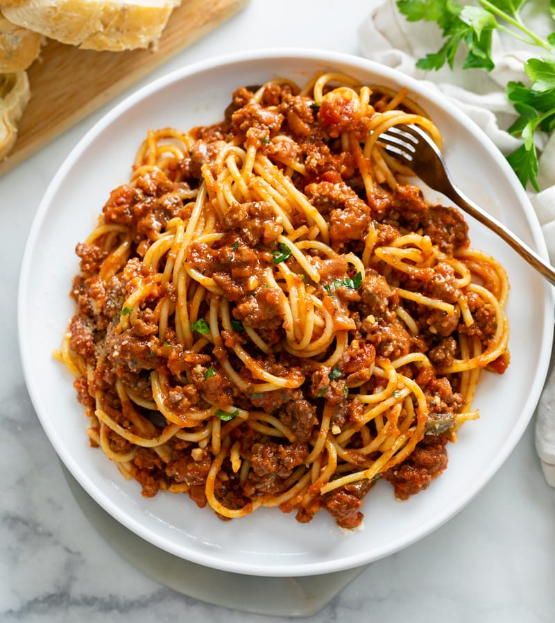 Spaghetti topped with Meat Sauce on a white plate with a fork and parsley on top.
