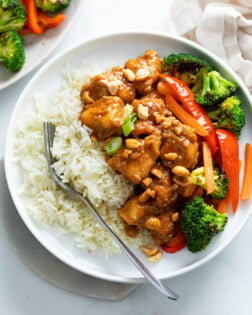 A white plate with rice and peanut butter chicken with stir-fried vegetables.