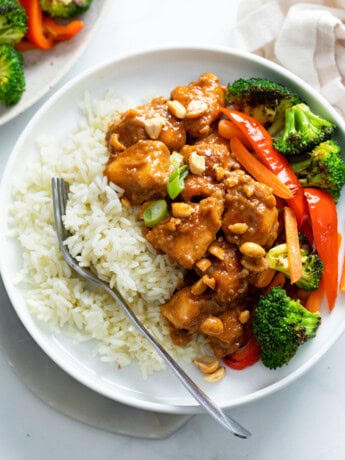 A white plate with rice and peanut butter chicken with stir-fried vegetables.