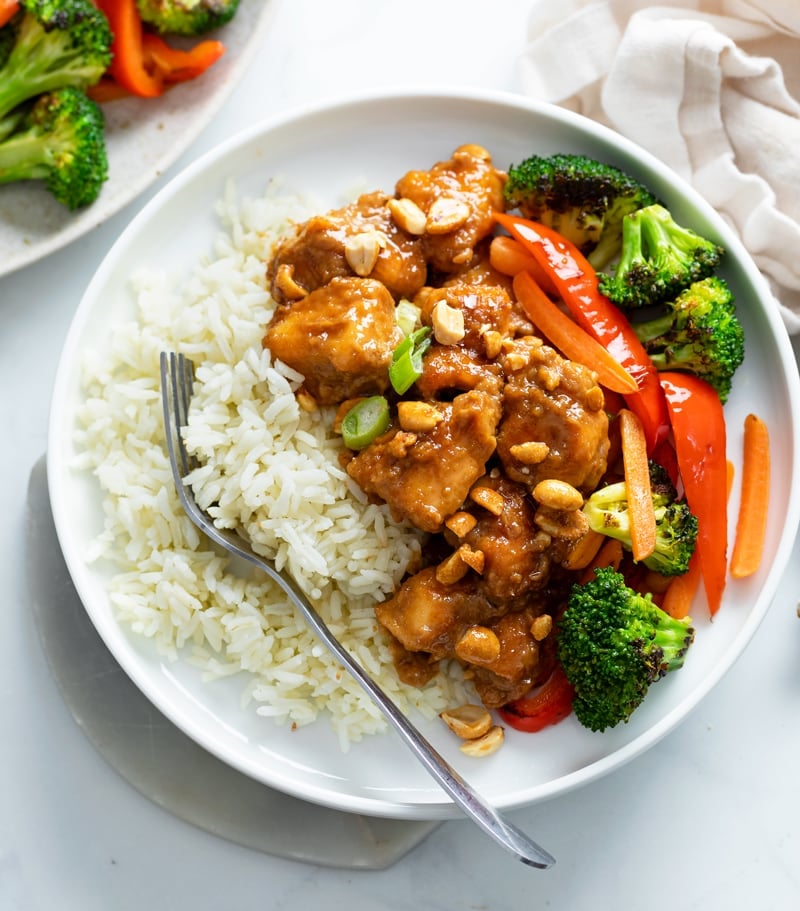 A white plate with rice and peanut butter chicken with stir-fried vegetables.