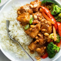 A white plate with Peanut Butter Chicken with white rice and vegetables.