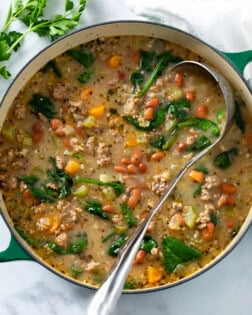 A green Dutch oven filled with Pinto Bean Soup with a soup ladle in it and fresh parsley on the side.