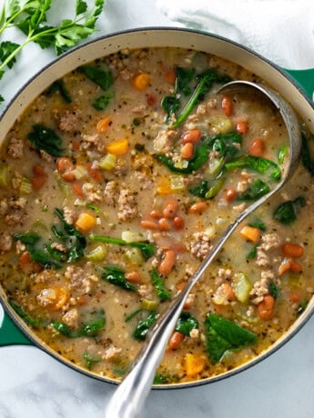 A green Dutch oven filled with Pinto Bean Soup with a soup ladle in it and fresh parsley on the side.