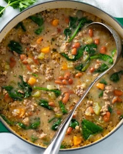 A soup pot filled with Pinto Bean Soup with a ladle and parsley on the side.