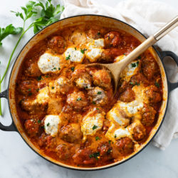 A skillet filled with Ricotta Meatballs in marinara sauce with herb ricotta on top.