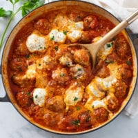 Ricotta Meatballs in tomato sauce with herb ricotta cheese and a wooden spoon.