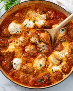 Ricotta Meatballs in tomato sauce with herb ricotta cheese and a wooden spoon.