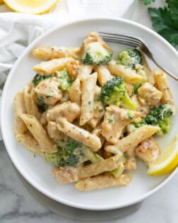 A white plate with Chicken and Broccoli Pasta and a lemon slice.