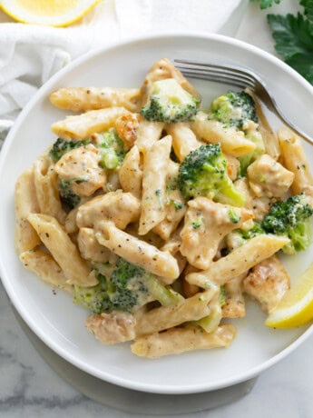 A white plate with Chicken and Broccoli Pasta and a lemon slice.