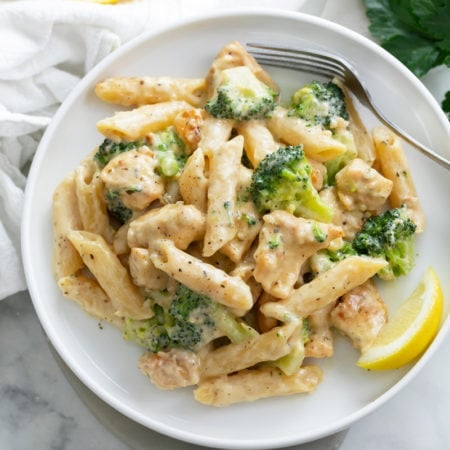 A white plate with Chicken and Broccoli Pasta and a lemon slice.